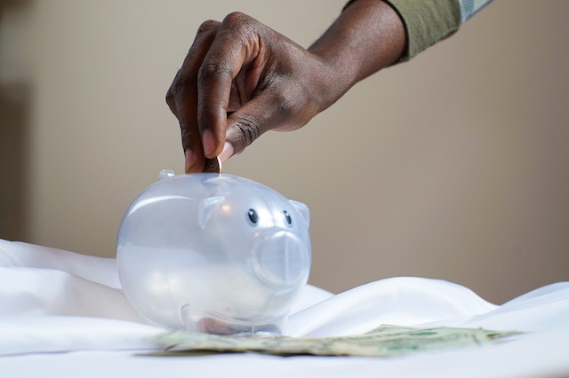 person placing coins into a clear piggybank